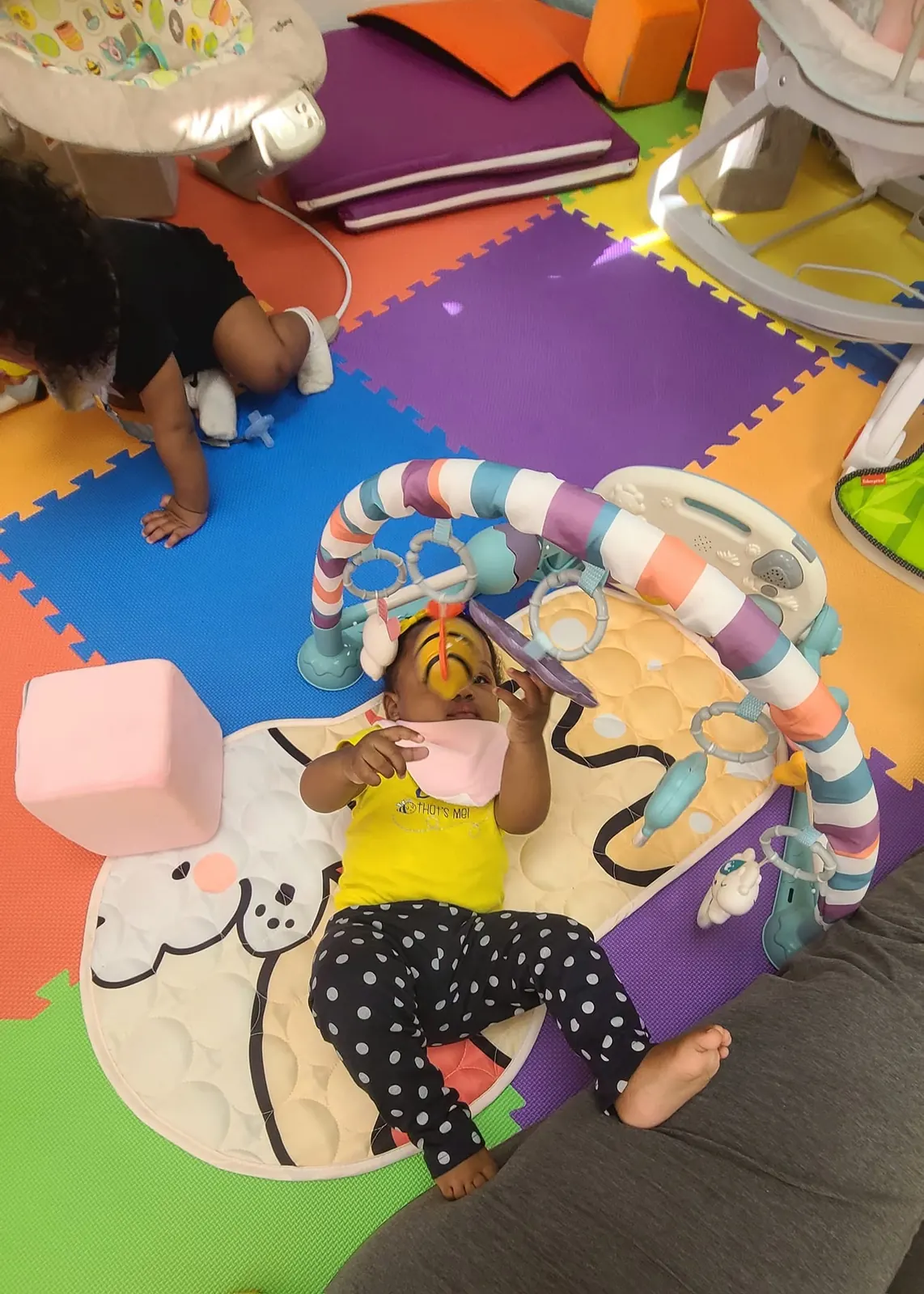Infant playing under an activity gym on a colorful foam mat